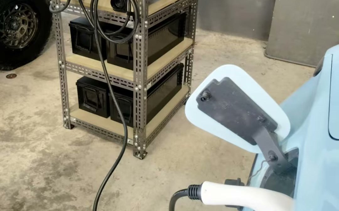 A rack of OCPH units in a garage, cabled to a Level 2 charger plugged into an electric car