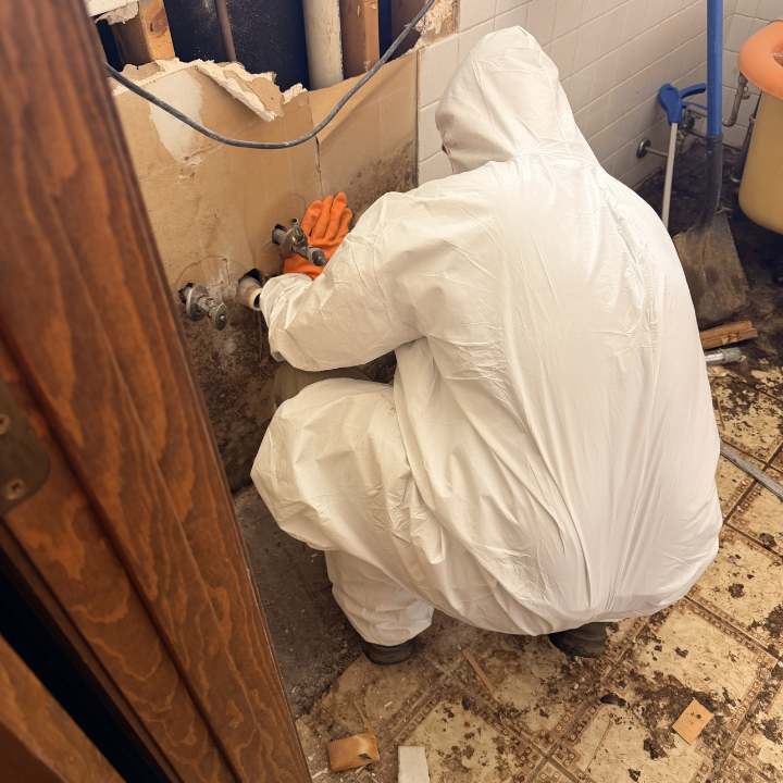Restoration technician in protective gear working near exposed plumbing during water damage cleanup Restoration technician in protective gear working near exposed plumbing during water damage cleanup