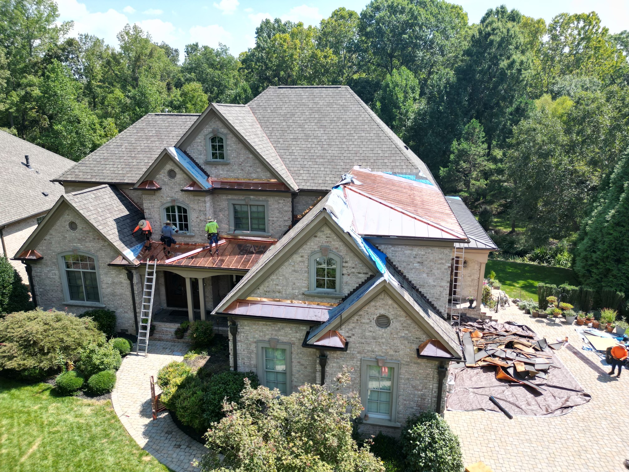 Crew installing standing seam metal over the front porch of a brick home, with the old roofing on a tarp in the driveway