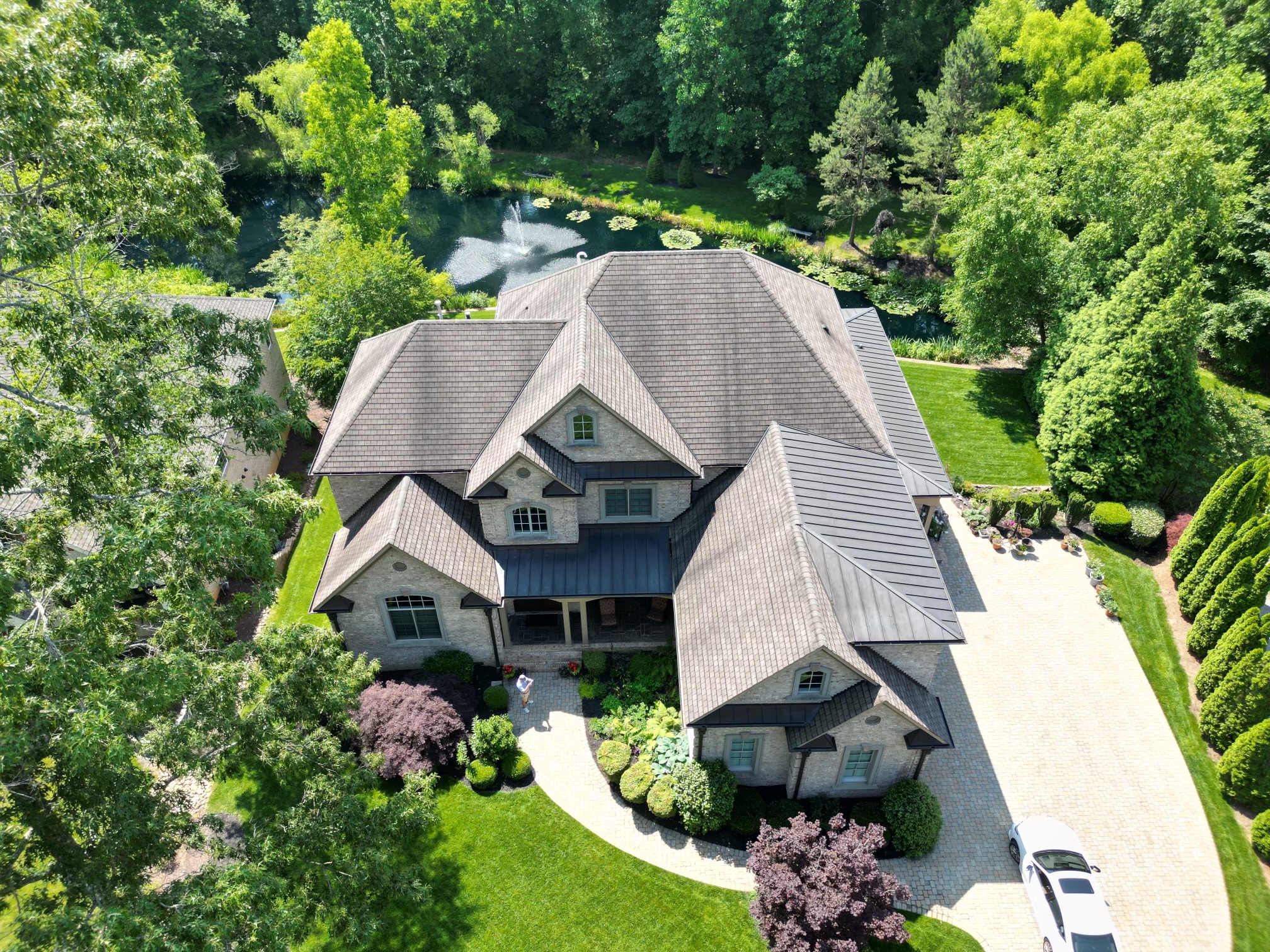 Aerial view of the finished brick home beside a pond, with a shingle roof and standing seam metal over the porch and side roofs