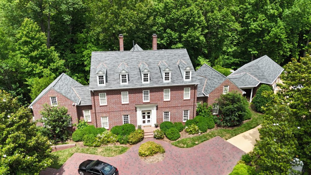 Aerial view of a red brick colonial home with a gray shingle roof, five dormers and two chimneys