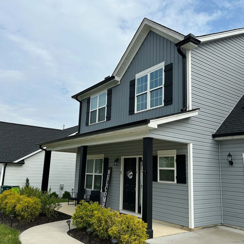 Two-story home with gray lap siding, board and batten siding on the front gable, black shutters and a covered front porch