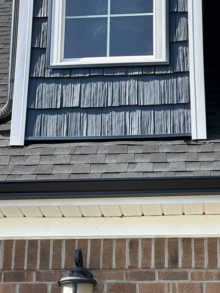 Close-up of dark gray shake-style siding on a dormer above a shingle roof, with white trim and new flashing at the roofline