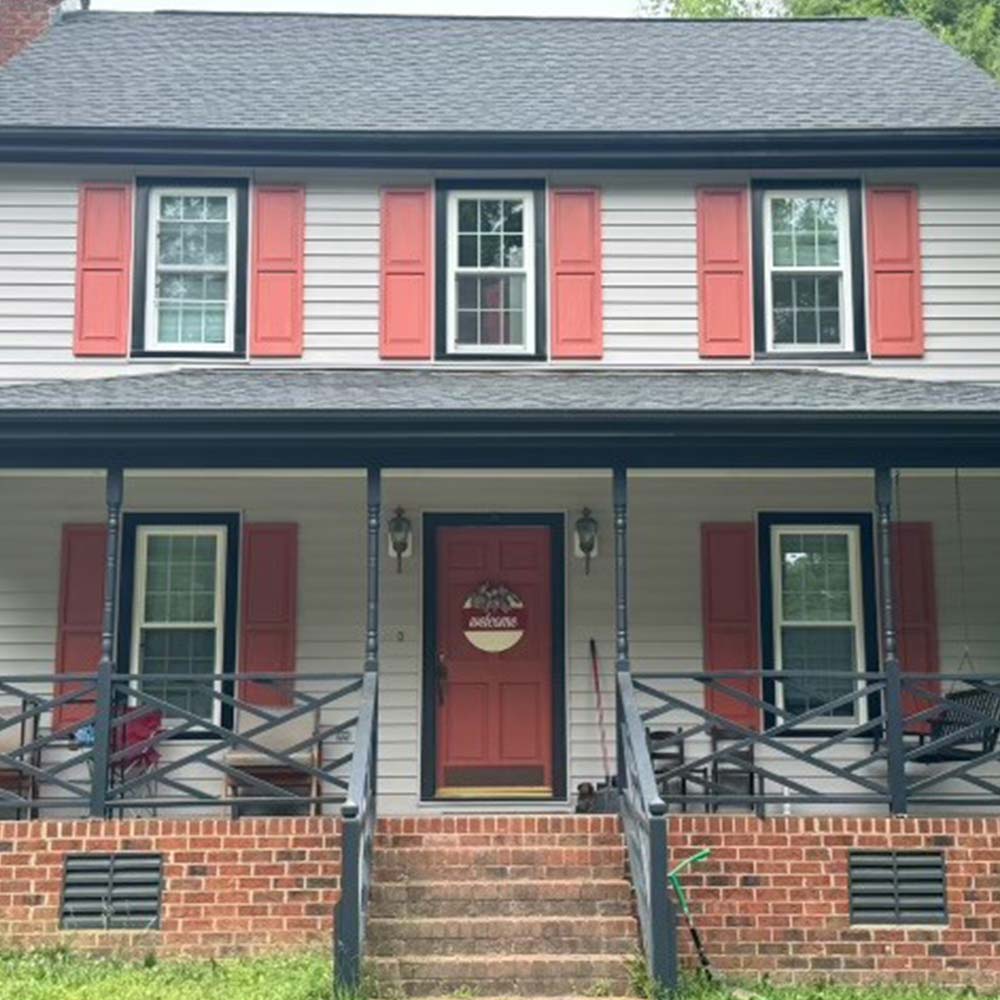 Two-story colonial with white lap siding, coral shutters, a dark-trimmed front porch and a brick foundation