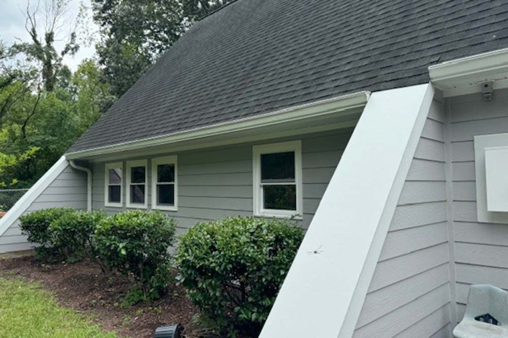 Gray lap siding wall with four white double-hung windows, white trim and gutters, under a dark shingle roof