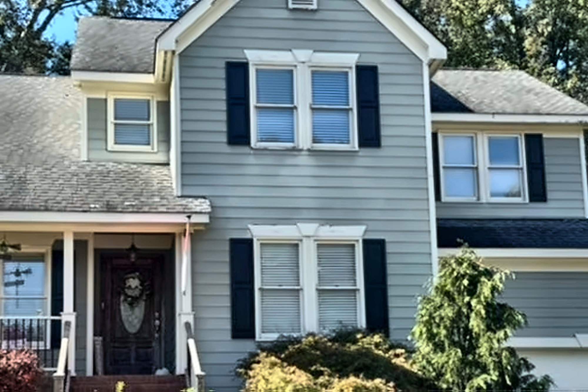 Before: the same home with blue-gray lap siding, white windows with navy shutters and an older gray shingle roof