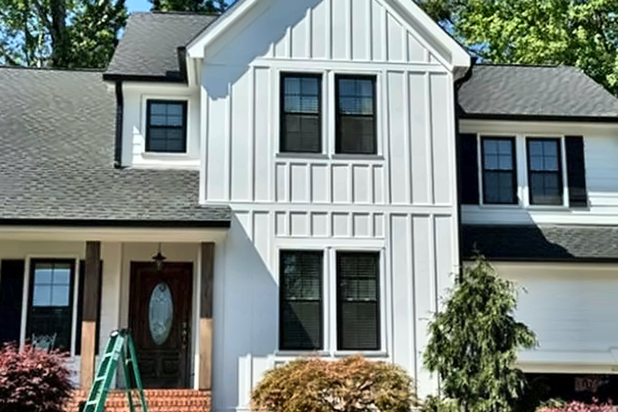After: two-story home with white board and batten and lap siding, black-framed windows, a dark shingle roof and wood porch posts