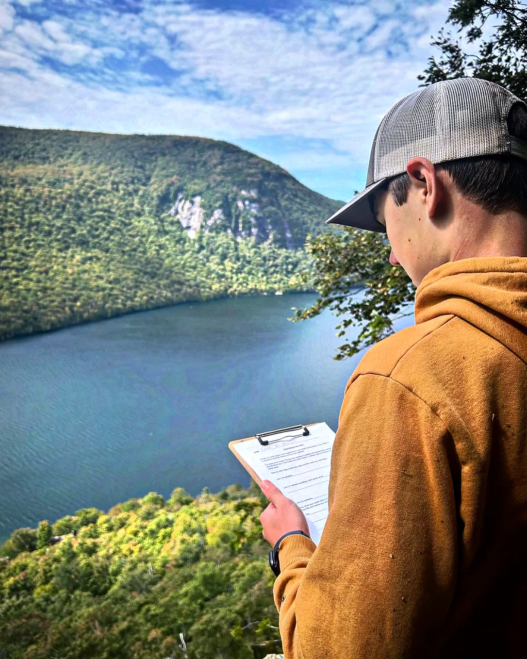 Student recording observations on a clipboard above Lake Willoughby