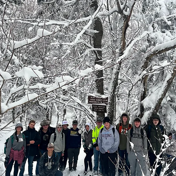 Large group of students beside a Bluff Mountain trail sign in a snow-covered forest