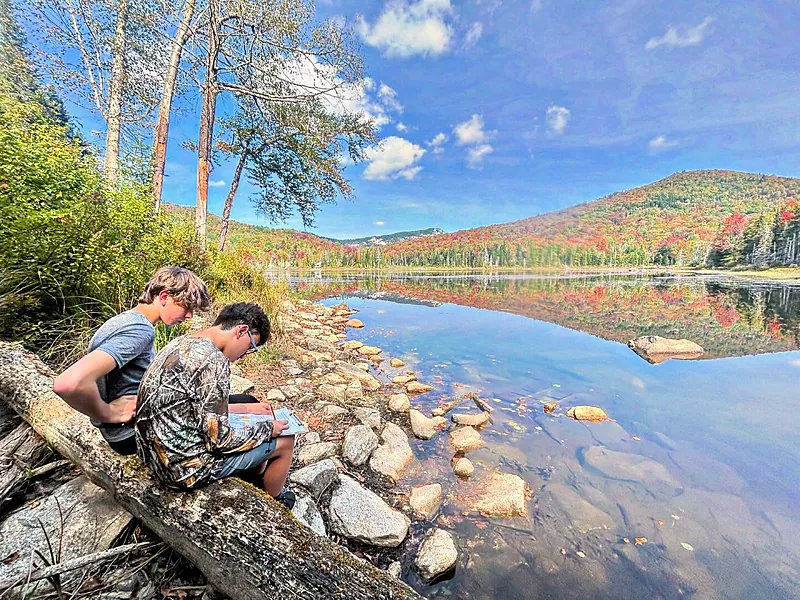 Two students studying a field guide on the shore of Wheeler Pond