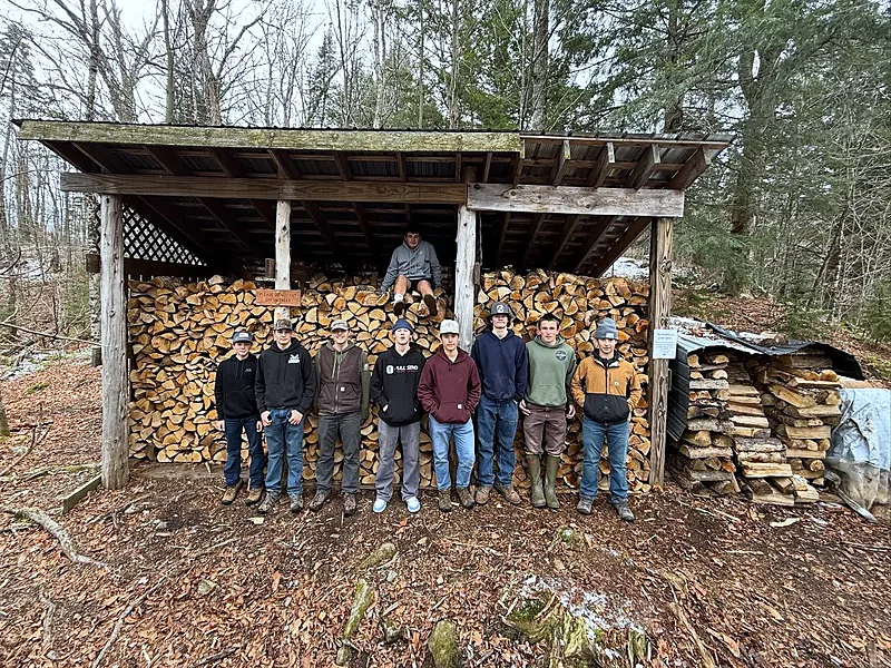 Students in front of a woodshed stacked with firewood they split during a service day