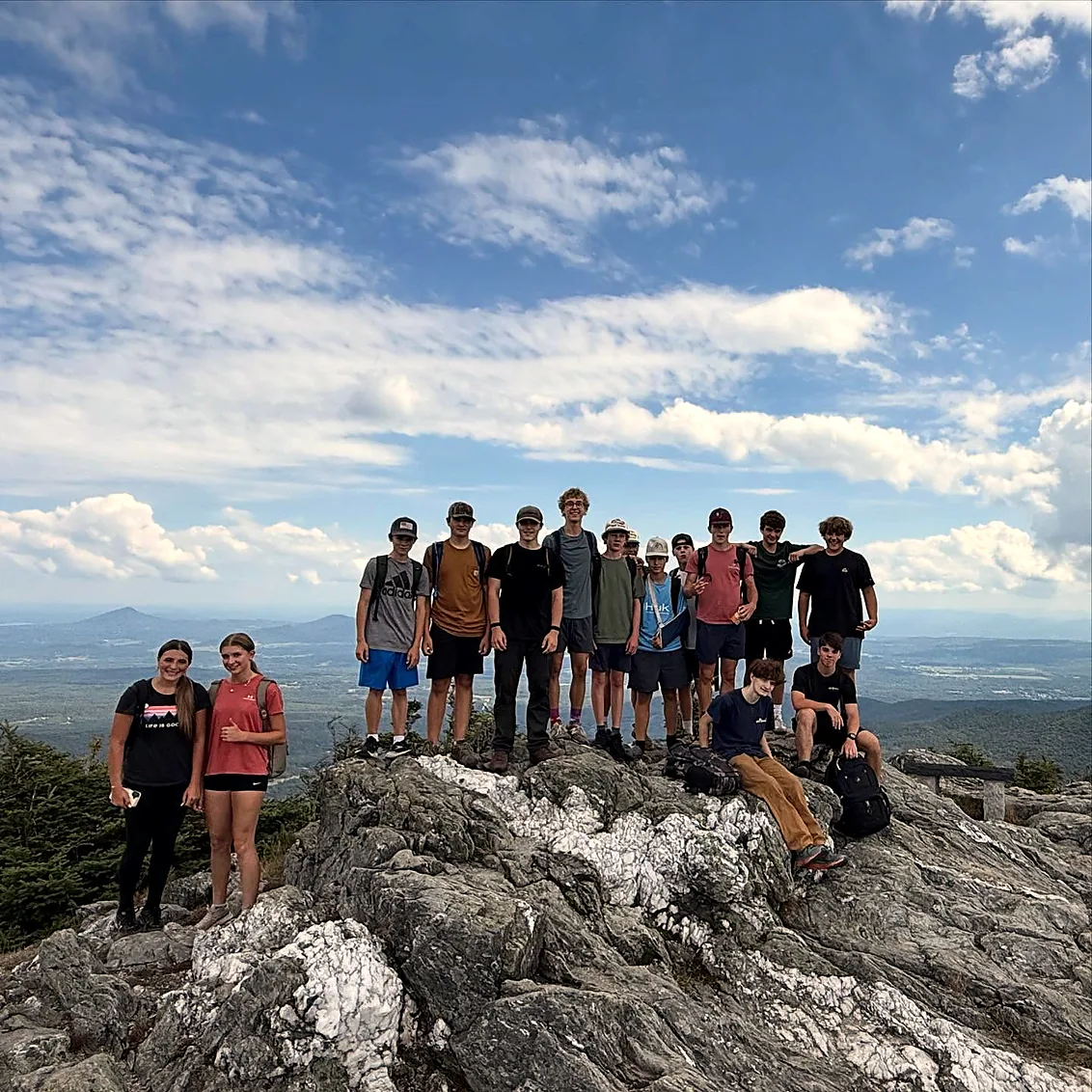 Group of students on a rocky Vermont summit under a wide blue sky