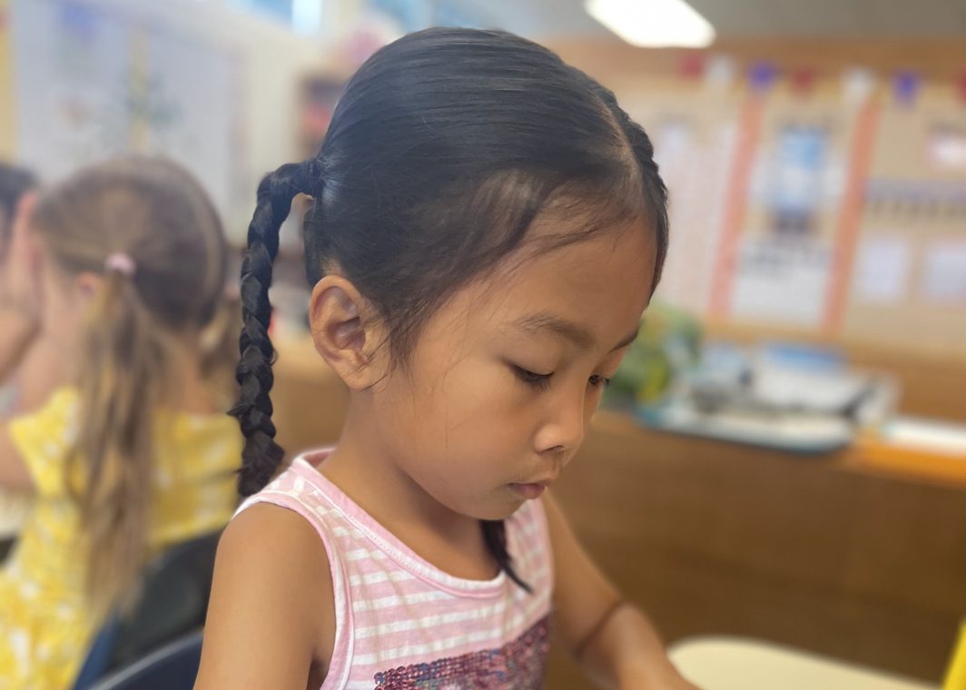 A girl with a braid concentrates on her work at a table in a Little Scholars classroom