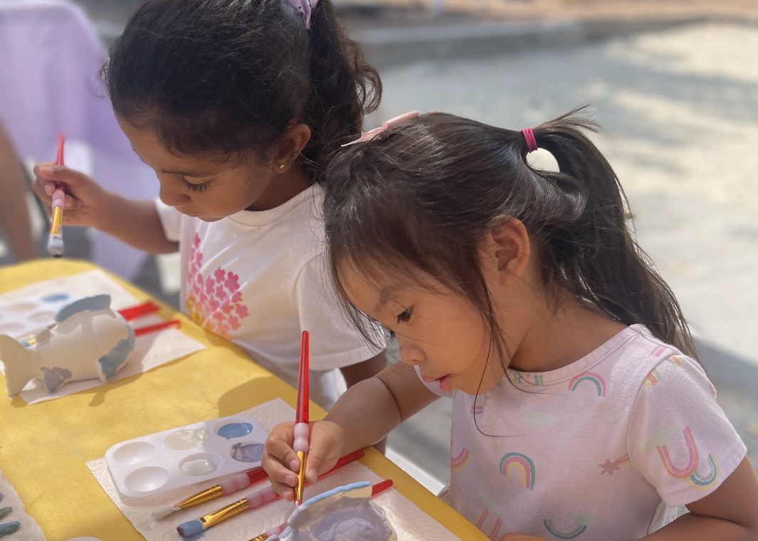 Two girls paint a plaster fish together at a yellow-covered table