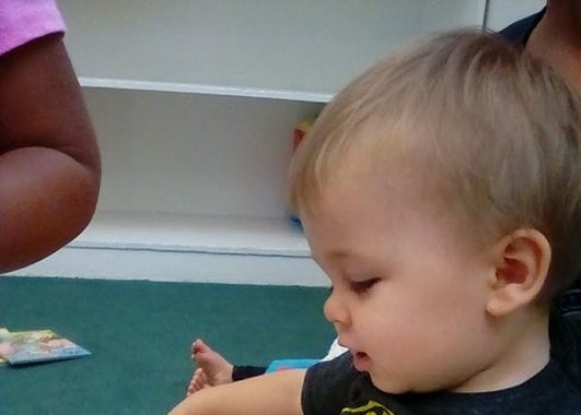 An infant looks at a board book in the Little Scholars infant room
