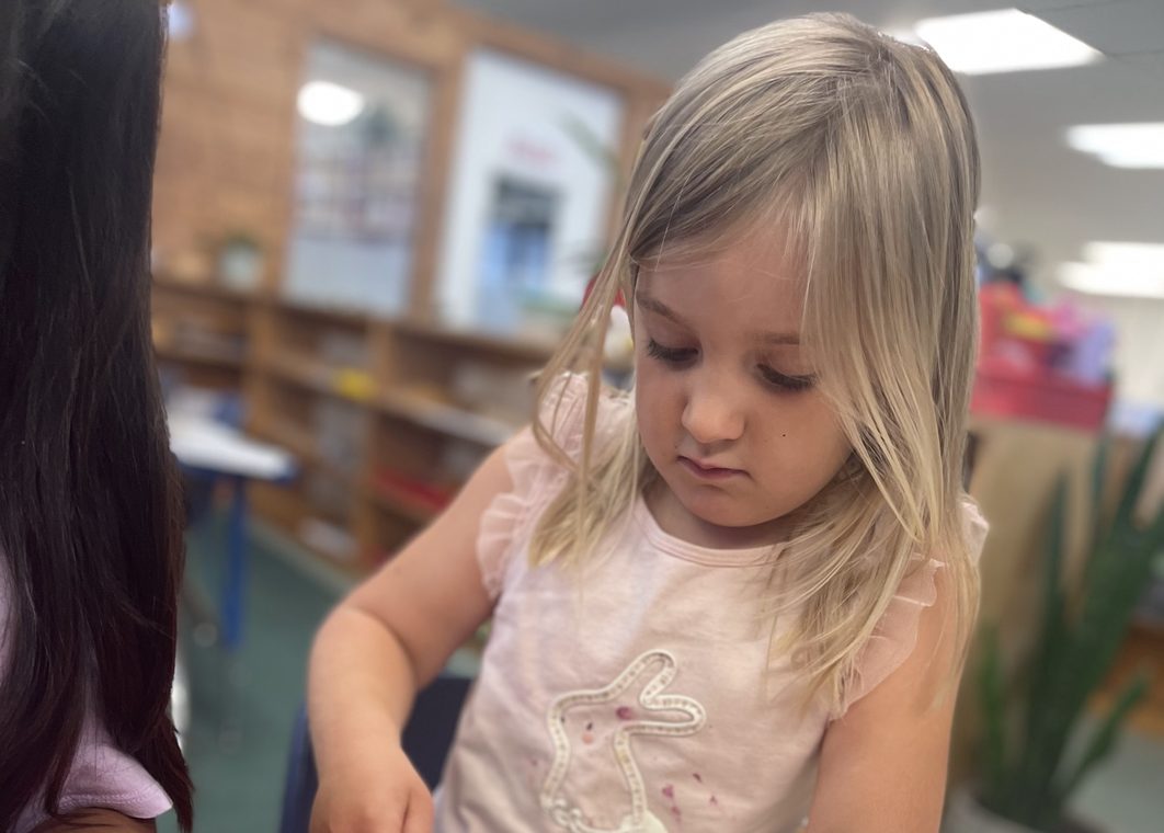 A preschool girl looks down in concentration at her work at a classroom table
