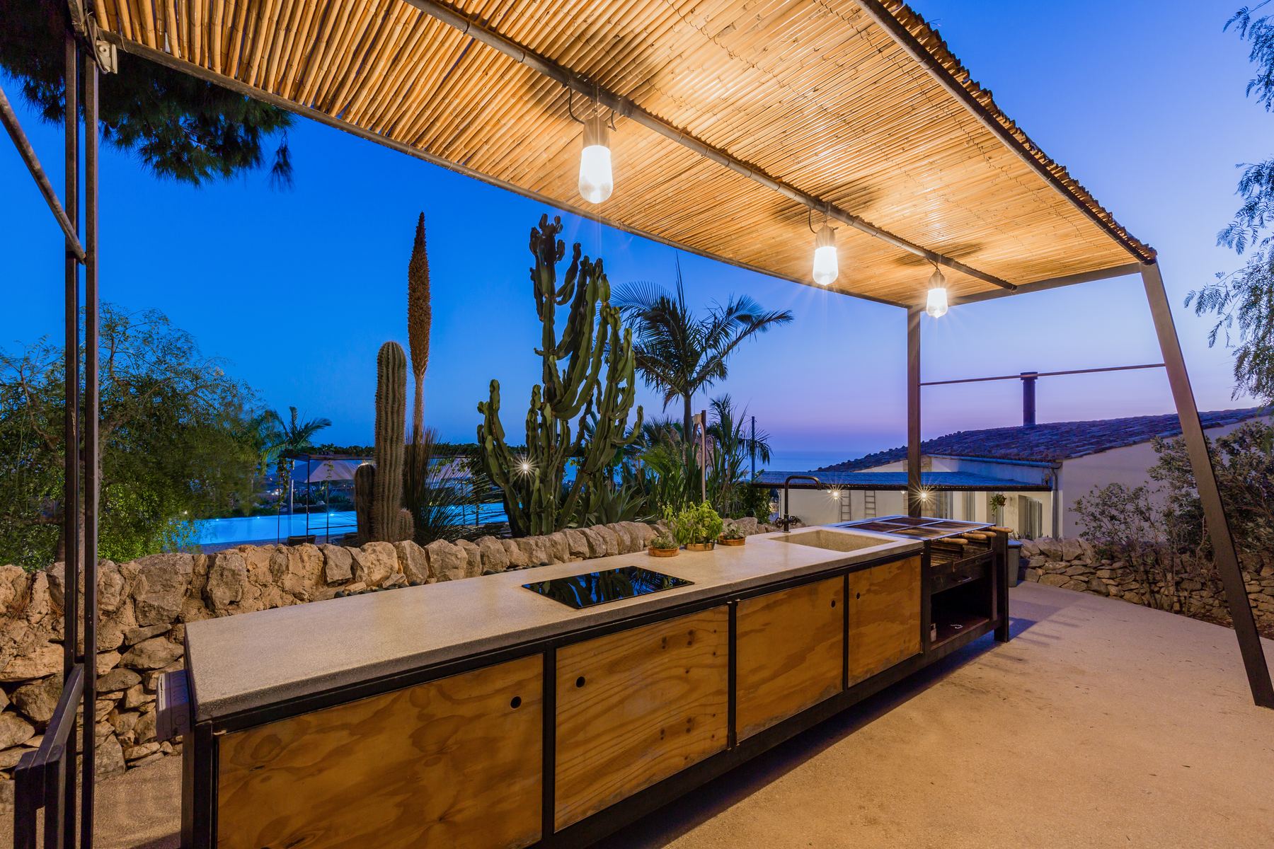 The outdoor kitchen under a reed pergola at dusk