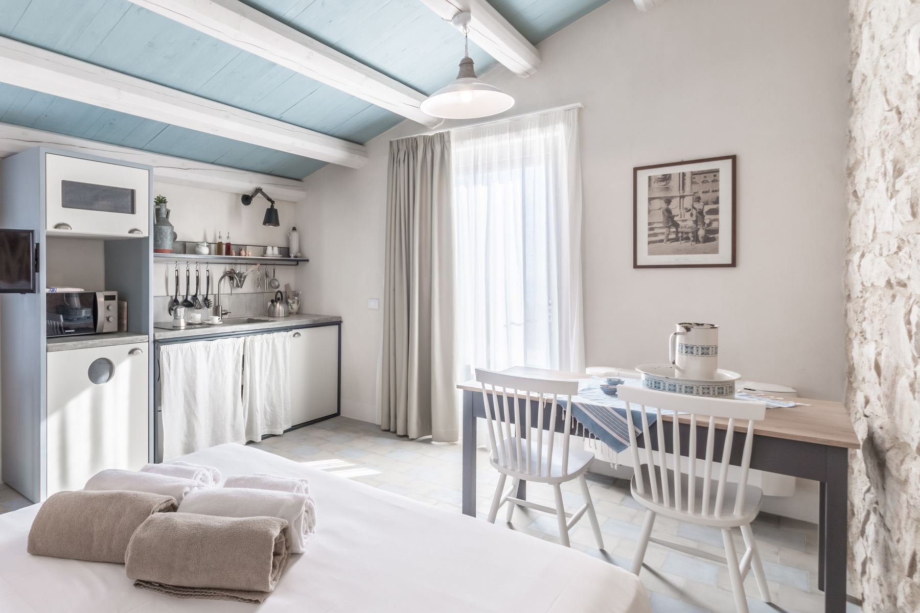 A room with a painted blue beamed ceiling and small kitchen