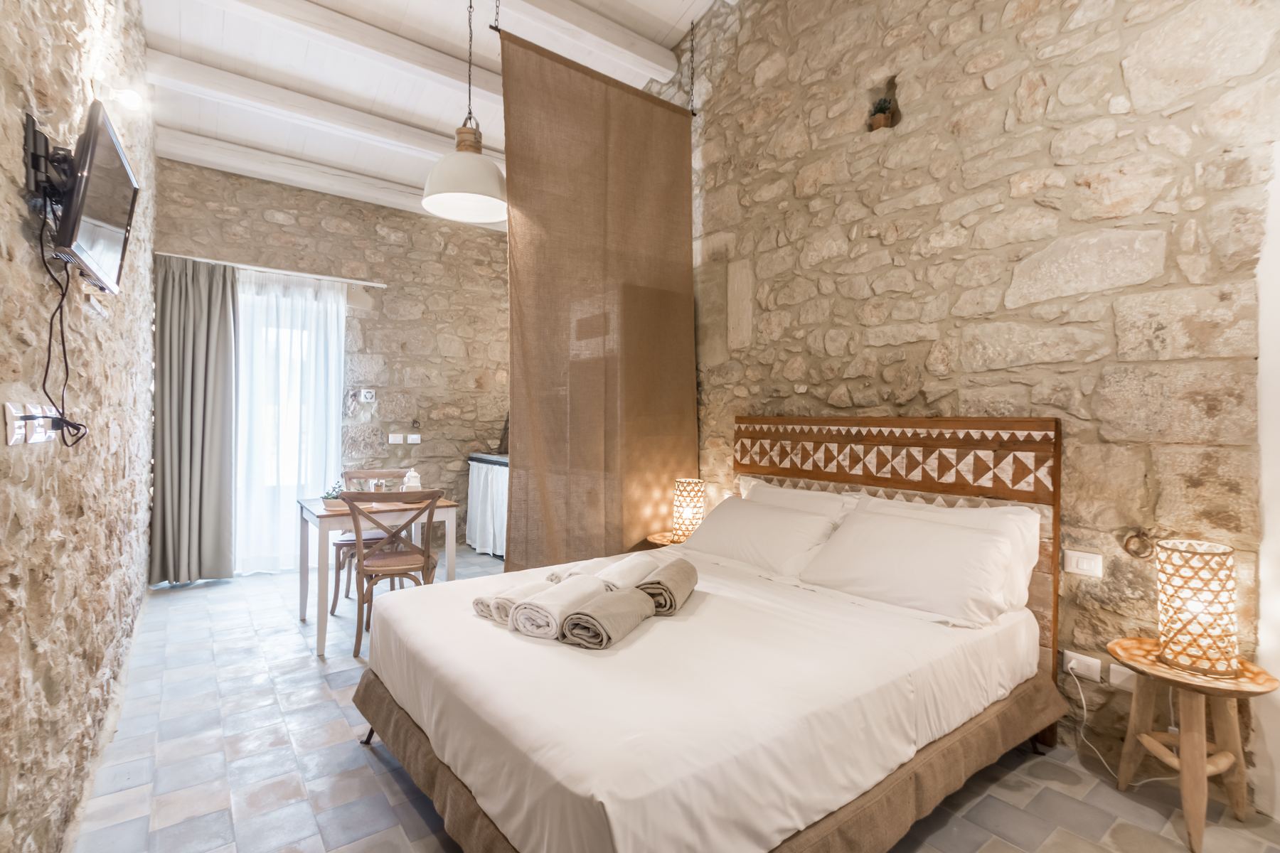 A stone-walled double room with a carved wooden headboard