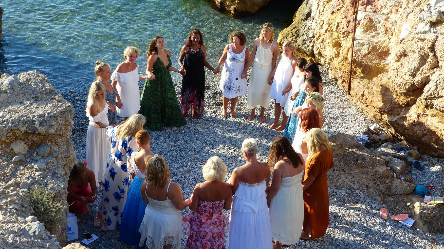 A circle holding hands on a pebble beach