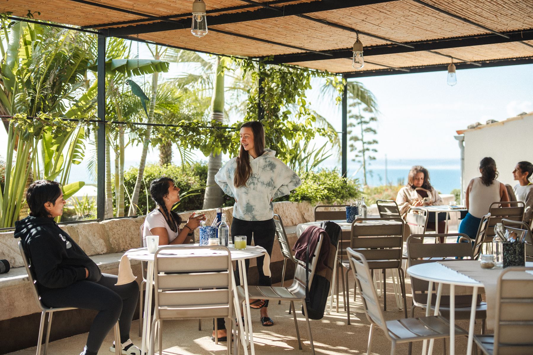 Guests laughing together under the pergola, sea beyond