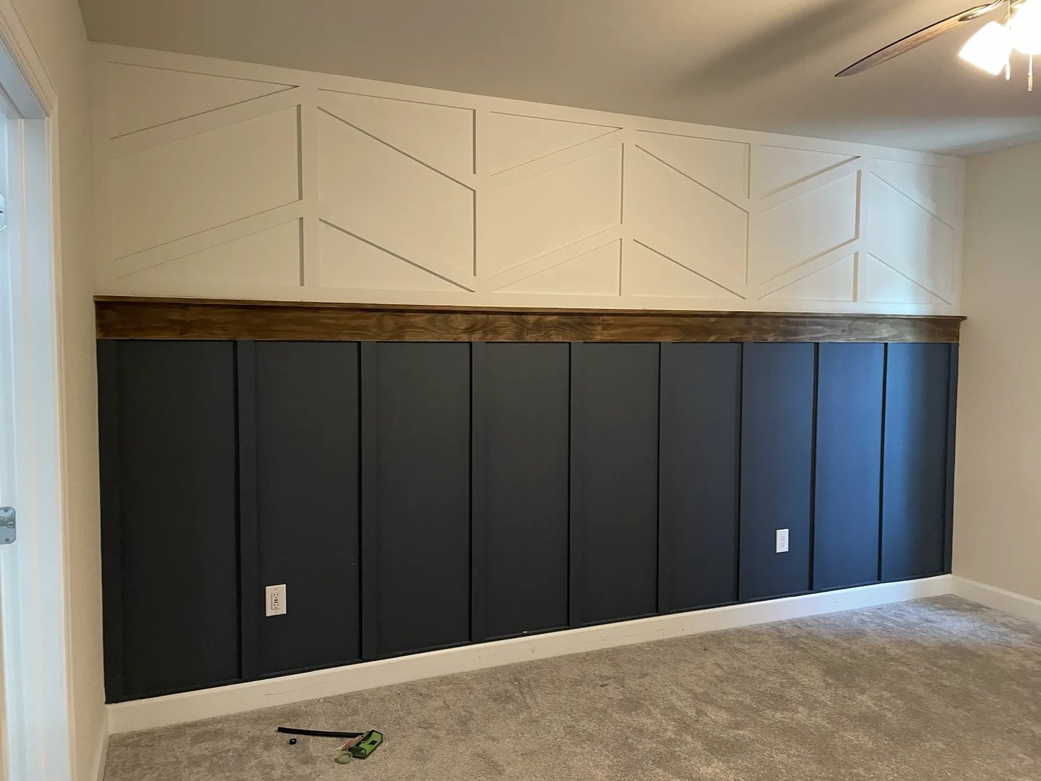 Geometric batten feature wall above navy board-and-batten wainscoting with a stained wood ledge