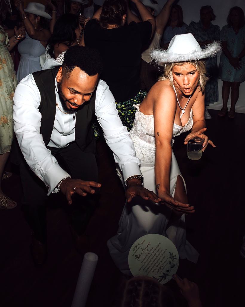 Bride in a white cowboy hat and groom getting low together on the dance floor