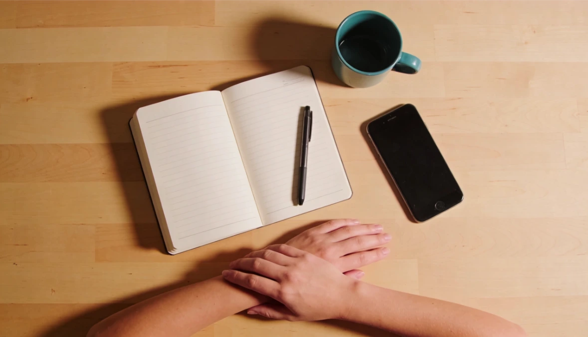 Overhead flatlay of notebook, pen and phone on light wood desk - researching Dubsado pricing options Overhead flatlay of notebook, pen and phone on light wood desk - researching Dubsado pricing options
