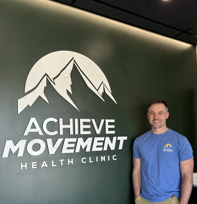 Dr. Steve Martinow beside the Achieve Movement logo wall inside the Simcoe clinic