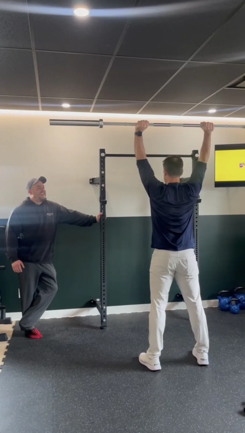 Patient holding a barbell overhead while a clinician spots at Achieve Movement Health Clinic in Simcoe