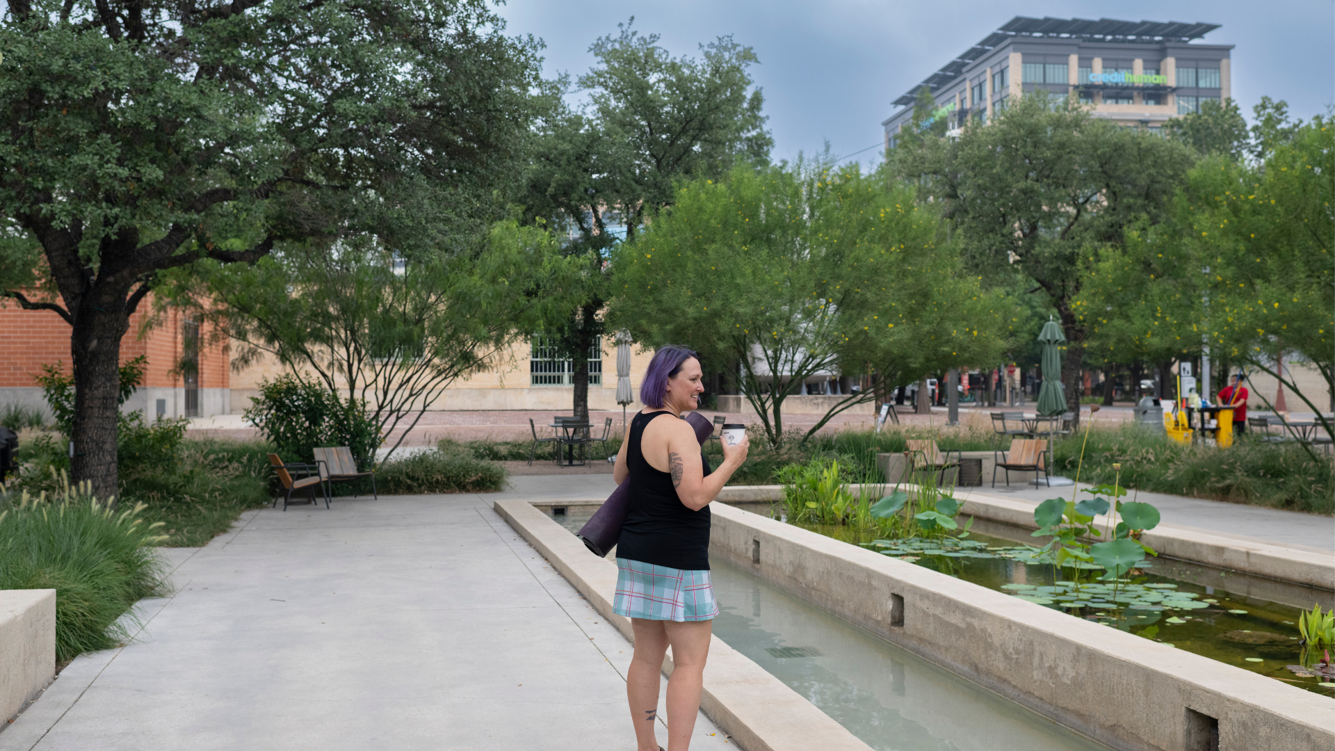 Eva ZobianWolf, trauma-informed yoga therapist and founder of Eva Zee Wellness, walking outdoors with a yoga mat and coffee cup, purple hair, in San Antonio Texas.