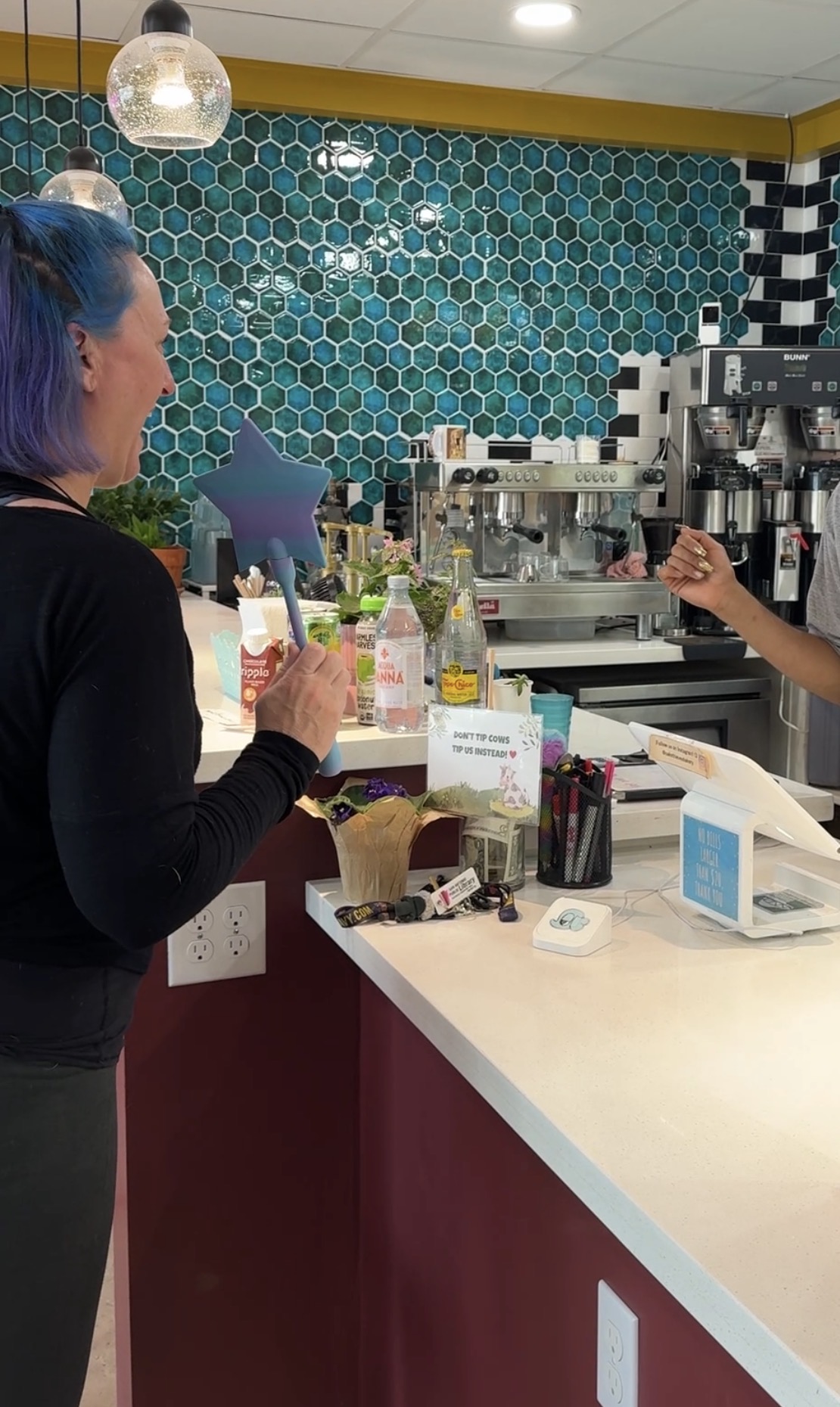 author standing with purple blue plastic fairy wand that holds a payment card and is being used to tap pay at a coffee/donut shop