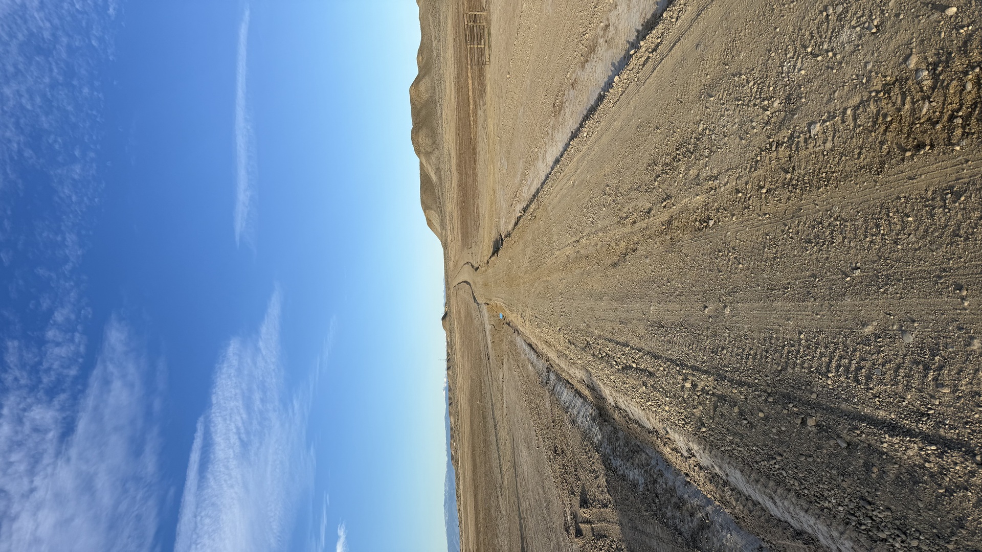 A motor grader leveling a rutted gravel driveway on a rural Fremont County, Wyoming property, with high-desert terrain visible in the background. The freshly graded surface shows a smooth, even slope with no visible potholes or washboard sections.