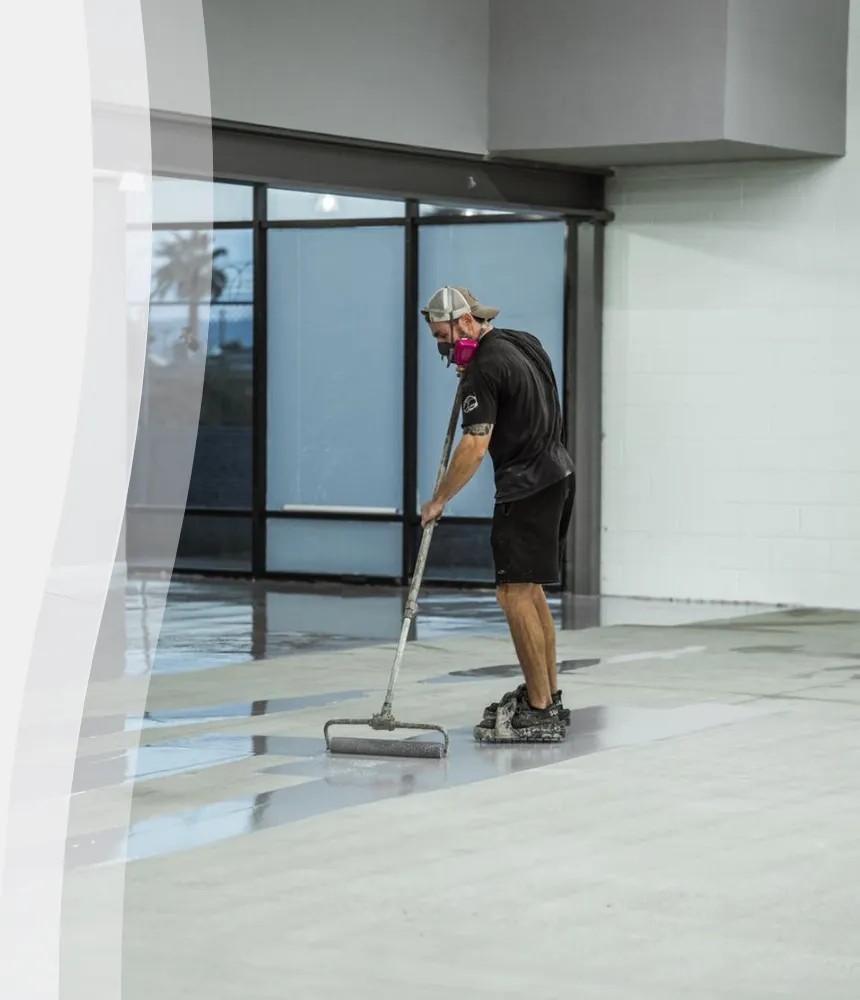 Epoxy flooring technician applying a smooth base coat to a commercial concrete surface during a floor coating installation.