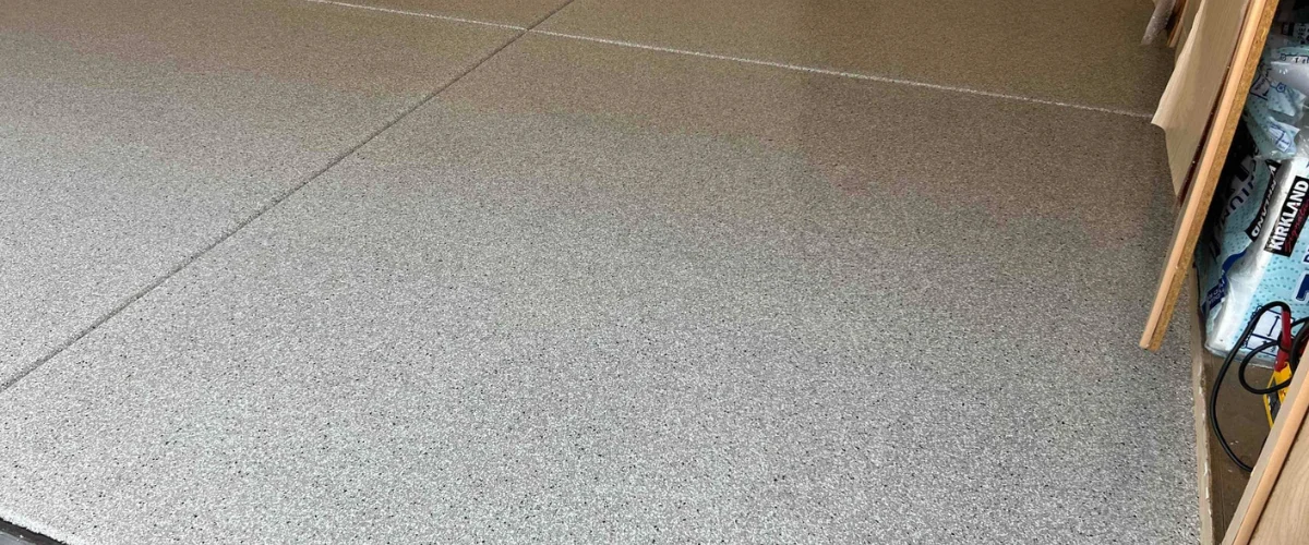 A gray epoxy-coated garage floor with visible seams, showing a granular texture and a shelf on the right.