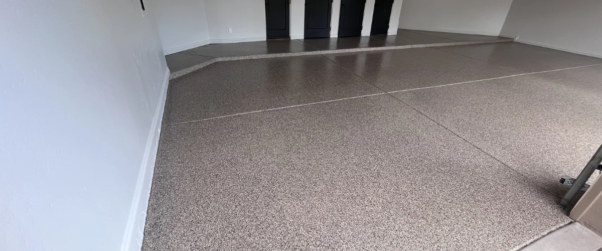 Close-up of a light tan epoxy garage floor with dark and white speckles, showing a shiny finish.