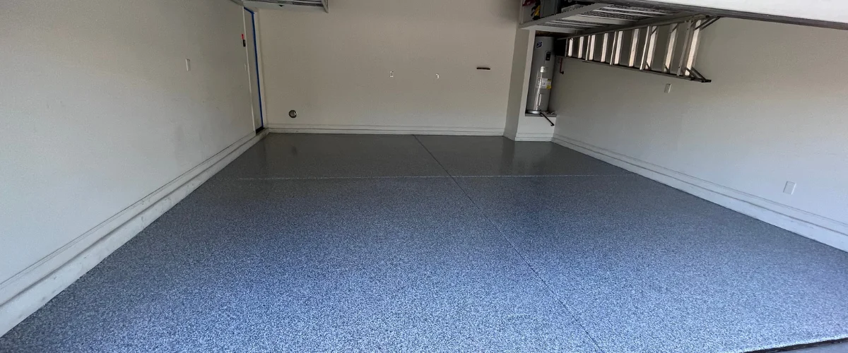 An empty two-car garage with new gray epoxy flake flooring, featuring a hot water heater and water softener. An empty two-car garage with new gray epoxy flake flooring, featuring a hot water heater and water softener.