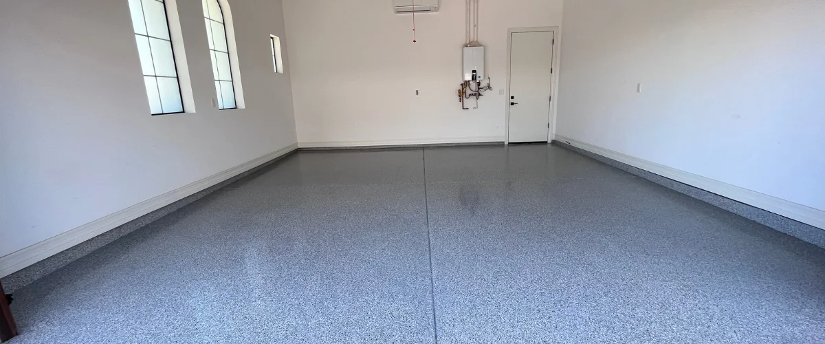 An empty garage with white walls and a newly installed blue and gray flecked epoxy floor coating. An empty garage with white walls and a newly installed blue and gray flecked epoxy floor coating.