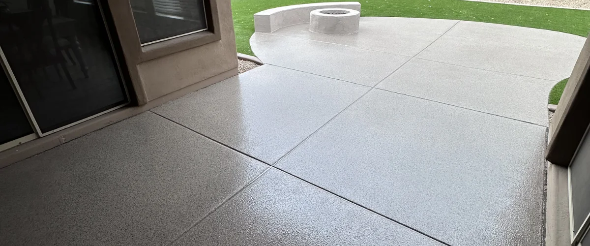 A newly coated concrete patio leading to a curved fire pit area and green artificial turf A newly coated concrete patio leading to a curved fire pit area and green artificial turf