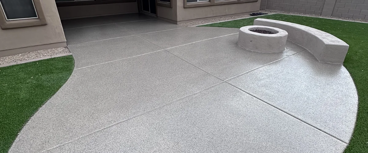 A modern backyard patio with textured gray flooring, a built-in fire pit, and artificial green turf. A modern backyard patio with textured gray flooring, a built-in fire pit, and artificial green turf.