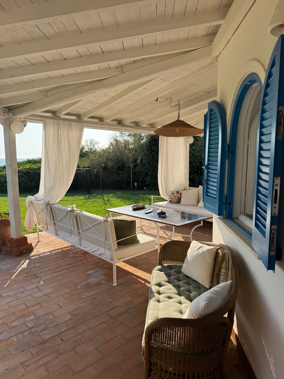 Portico con travi bianche, tende di lino, pavimento in cotto e persiane blu — villa a Sabaudia