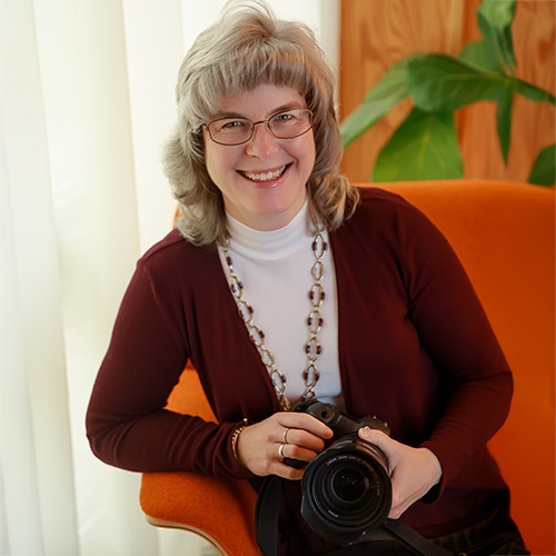 Lisa Jenkins, St. Louis portrait photographer, smiling in an orange chair while holding her camera