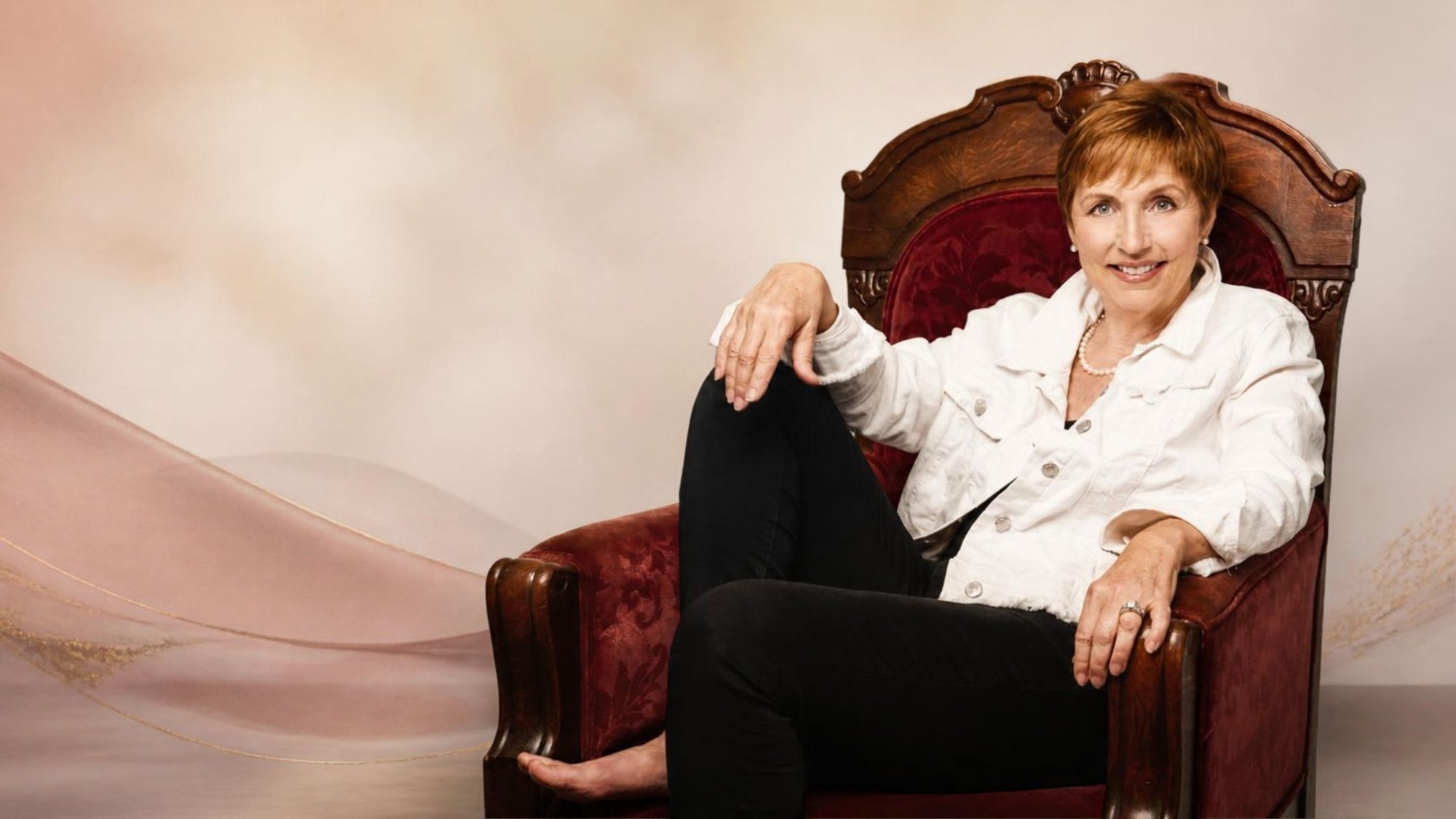 Laurette DeJulian smiling, seated in a carved red velvet chair