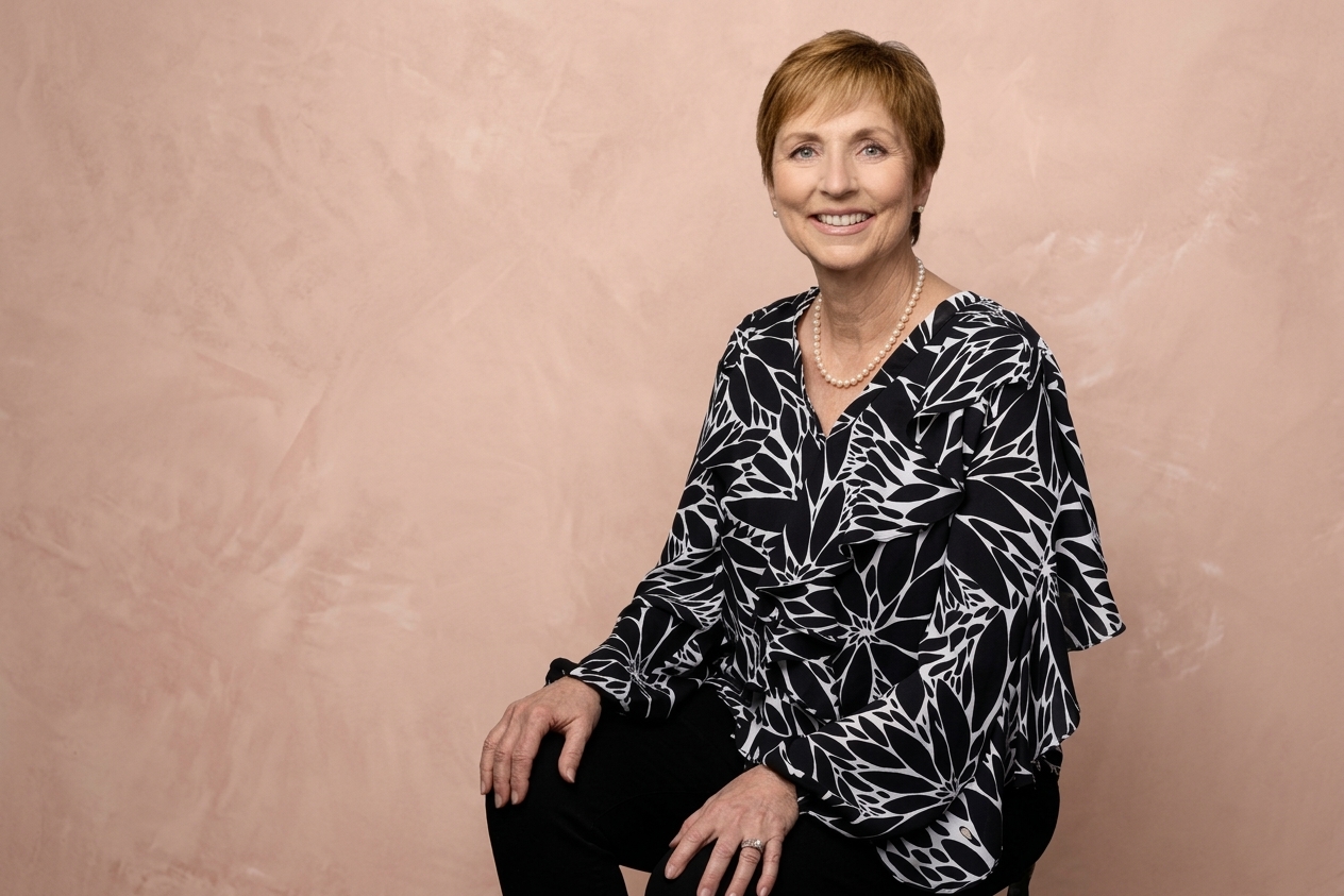 Laurette DeJulian seated, smiling, in a black and white floral blouse and pearls