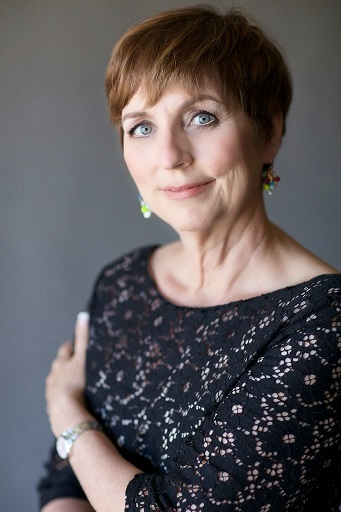 Laurette DeJulian in a black lace top, arms folded, smiling