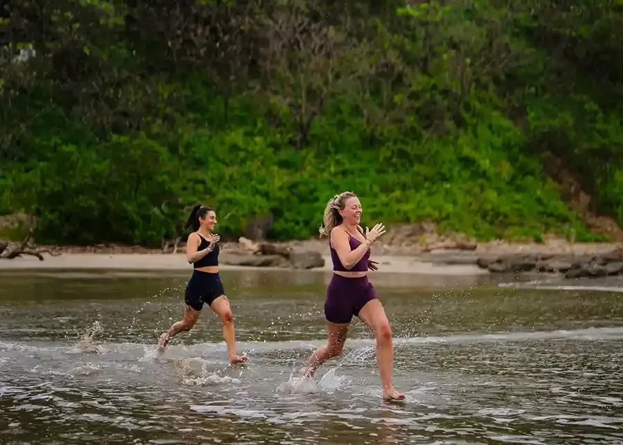 Two women running out of the ocean laughing