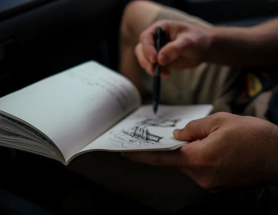 A hand sketching a house in pencil in an open sketchbook