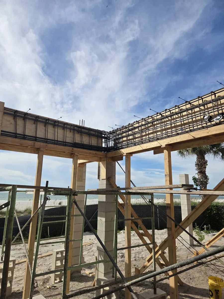 The timber frame of a raised coastal home on concrete columns, palms beyond