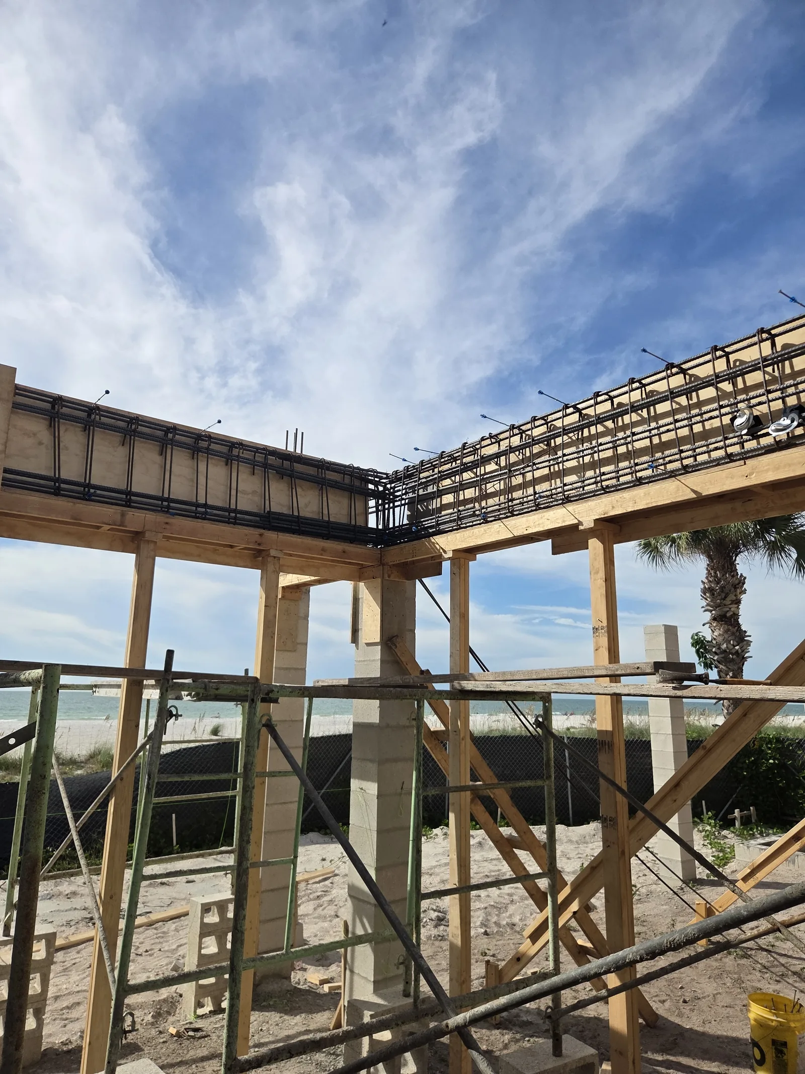 The timber frame of a raised coastal home on concrete columns, palms beyond