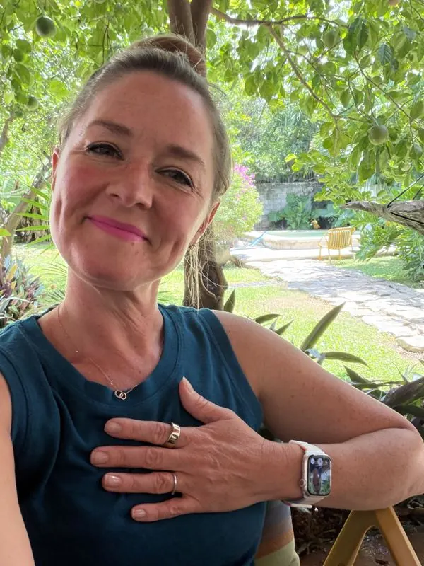 Anya Gossage smiling in a sunny garden with her hand on her chest, wearing her Oura Ring